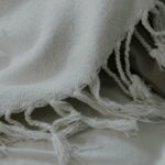 Plaid en coton naturel blanc avec franges, posé sur un lit doux, illustrant les matières naturelles idéales pour bébé