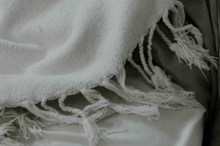 Plaid en coton naturel blanc avec franges, posé sur un lit doux, illustrant les matières naturelles idéales pour bébé