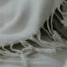 Plaid en coton naturel blanc avec franges, posé sur un lit doux, illustrant les matières naturelles idéales pour bébé