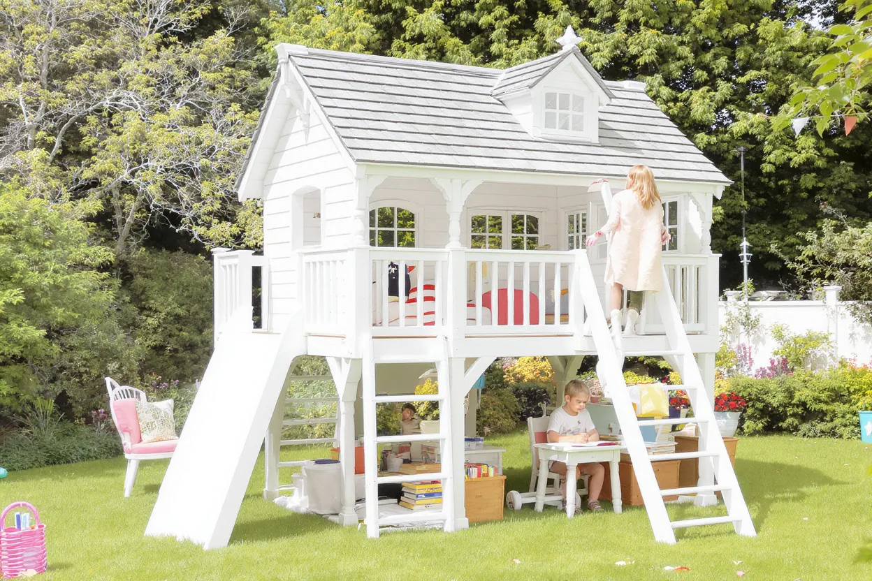 Lit cabane en extérieur surélevé évolutif en bois blanc, avec bureau intégré et rangements, enfant de 7 ans lisant.